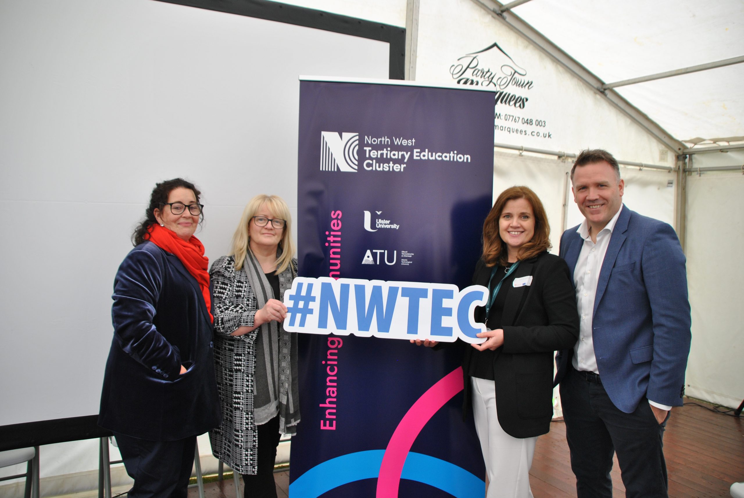 Four individuals standing in front of the North West Tertiary Education Cluster blue and white pull up holding NWTEC Hash tag sign