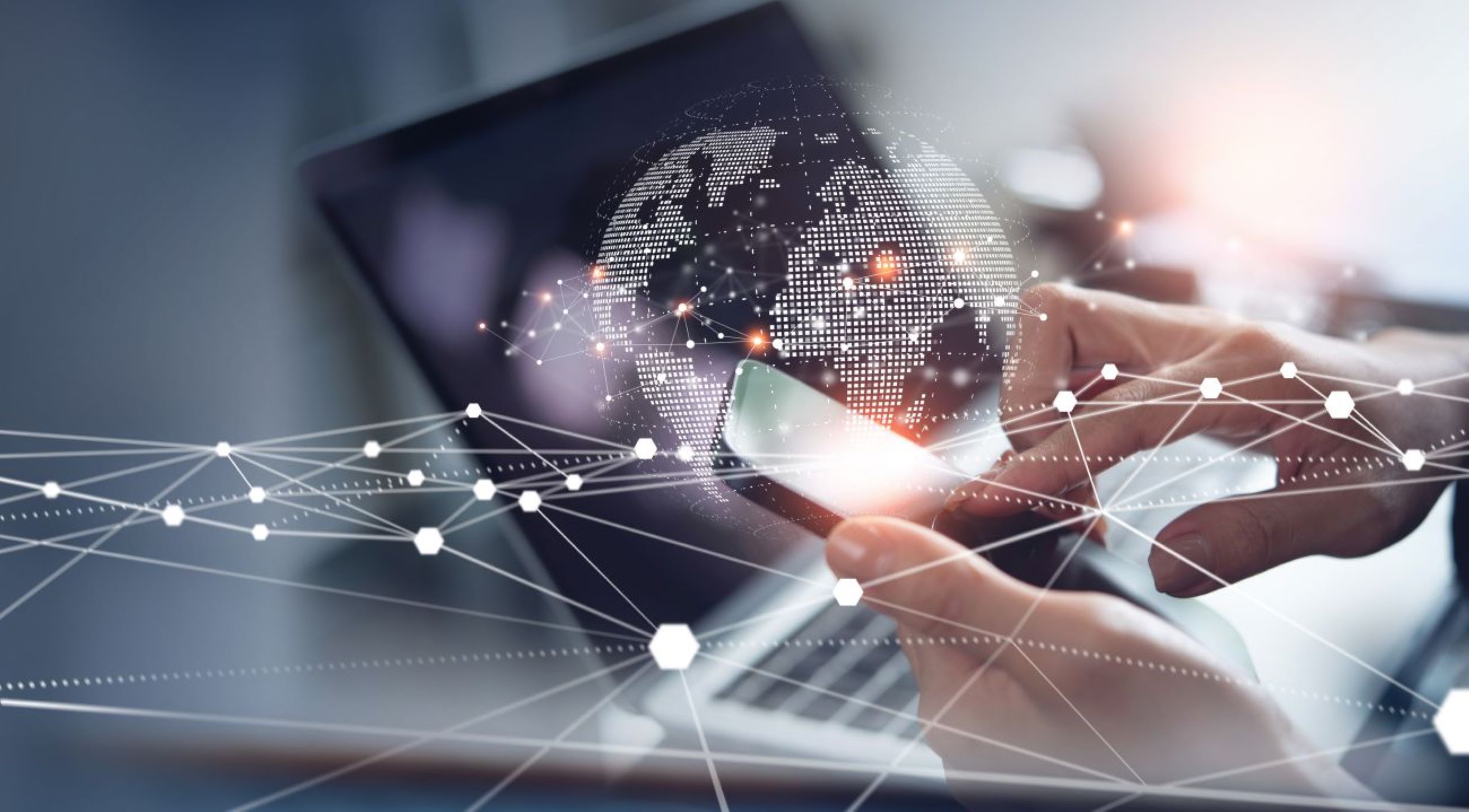 Pair of hands holding mobile phone over a laptop with the globe