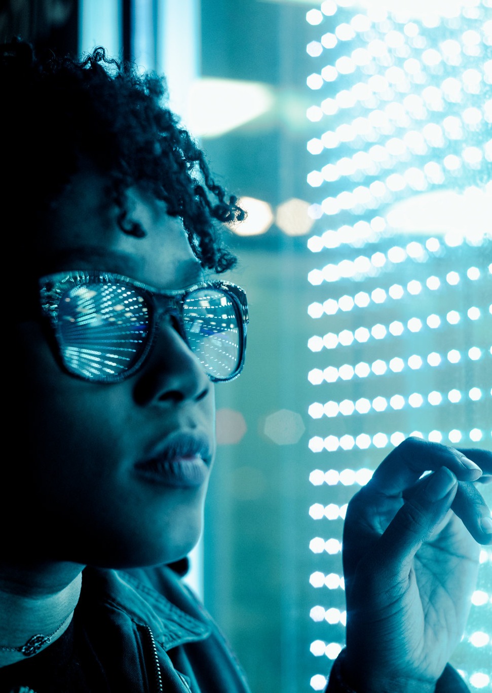 Young person wearing glasses touching an interactive user screen with light green lights reflecting on their glasses